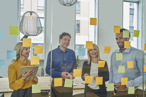 Business professionals brainstorming over adhesive notes on glass - AKLF00447