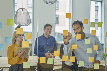 Businessman writing on adhesive note while discussing with colleagues in office - AKLF00448