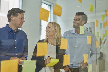 Business professionals having discussion seen through glass at office - AKLF00452