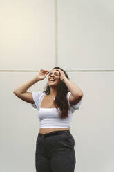 Young woman laughing with eyes closed in front of white wall - MTBF01057