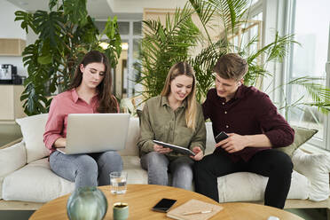 Lächelnde Praktikantin, die über ein digitales Tablet mit einem Geschäftsmann diskutiert, während sie neben einer Kollegin im Büro sitzt - AKLF00494