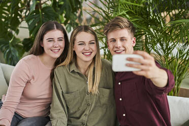 Lächelnder Geschäftsmann nimmt Selfie durch Handy mit weiblichen Kollegen im Büro - AKLF00506