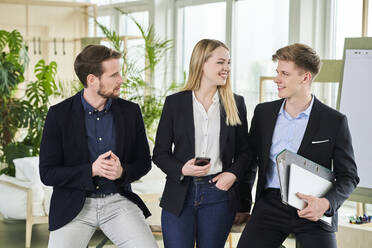 Smiling teenage intern discussing with male colleagues in office - AKLF00526