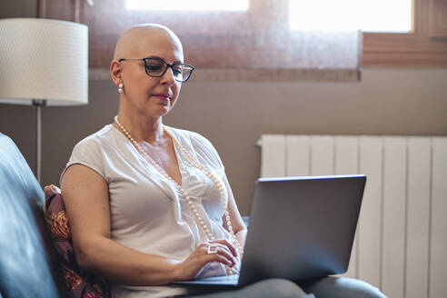 Bald woman using laptop in living room at home - AGOF00197