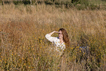 Smiling young woman shielding eyes while looking away on field - EIF02005