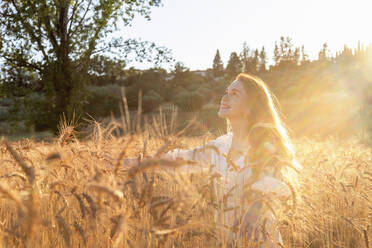 Lächelnde Frau genießt den sonnigen Tag inmitten von Weizenpflanzen auf einem Feld - EIF02015