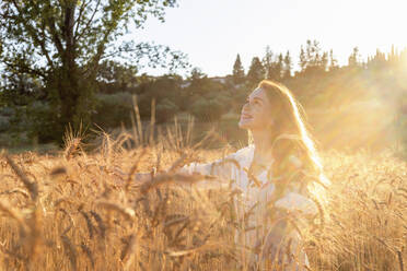 Smiling woman enjoying sunny day amidst wheat plants on field - EIF02015