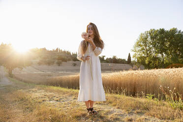 Junge Frau bewundert eine Knoblauchblüte auf einem Weizenfeld an einem sonnigen Tag - EIF02020