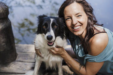 Glückliche Frau mit Border Collie auf dem Steg sitzend - EBBF04446