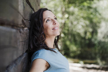 Smiling mid adult woman looking away while leaning on wall - EBBF04461