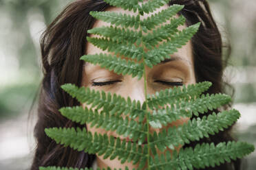 Woman with eyes closed behind green fern leaf - EBBF04469