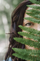 Mid adult woman behind green fern leaf - EBBF04470