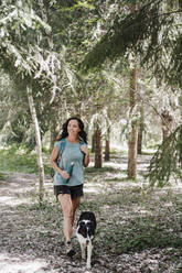 Woman hiking with Border Collie in forest - EBBF04473