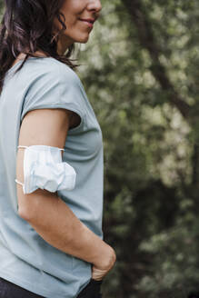 Stehende Frau mit Hand in der Tasche und Gesichtsschutzmaske am Arm im Wald - EBBF04475