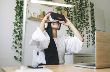 Young female professional using virtual reality simulator at home office - JCCMF03457