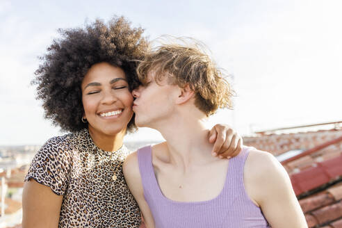 Young male kissing Afro female friend on cheek at rooftop during party - IFRF00981