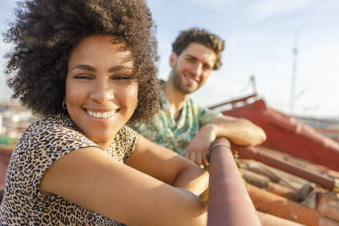 Lächelnde junge Frau und Mann auf der Terrasse an einem sonnigen Tag - IFRF00993