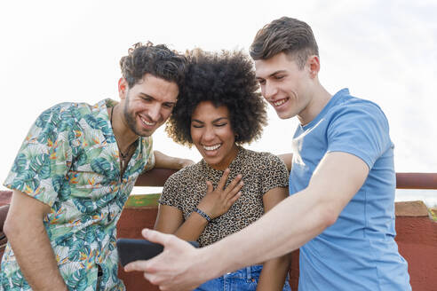 Junge männliche und weibliche Freunde lachen, während sie auf ihr Smartphone schauen - IFRF00995