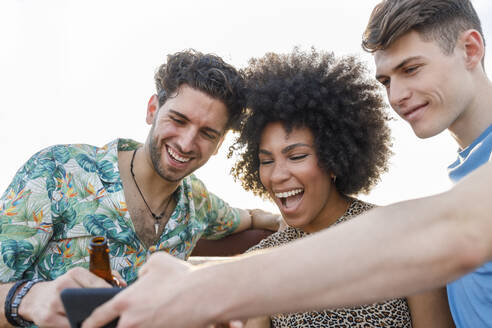 Fröhliche männliche und weibliche Freunde teilen sich ein Smartphone während einer Wochenendparty - IFRF00998
