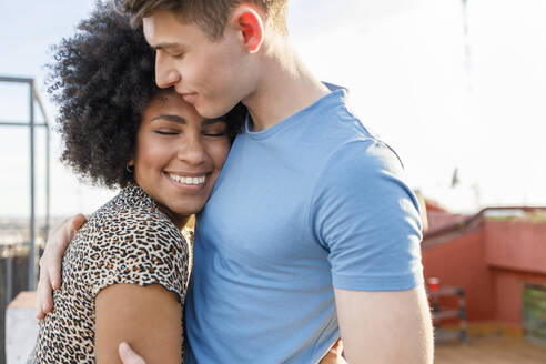 Lächelnde junge Frau umarmt ihren Freund auf der Terrasse - IFRF01010