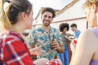 Junge männliche und weibliche Freunde, die während einer Party auf dem Dach etwas trinken - IFRF01013