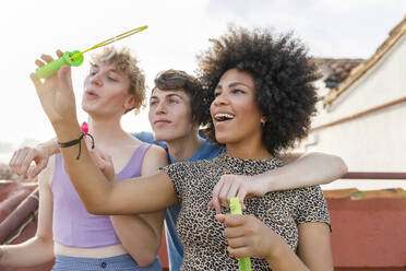 Junge multiethnische Freunde spielen mit Seifenblasen auf der Terrasse während einer Party - IFRF01019