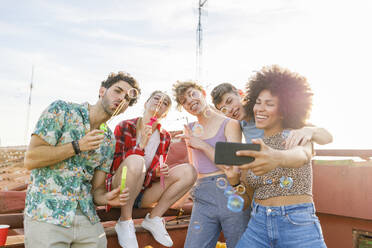 Fröhliche multiethnische Freunde machen ein Selfie beim Spielen mit Seifenblasen auf der Terrasse - IFRF01024