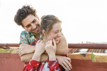 Young man embracing cheerful girlfriend on rooftop during weekend - IFRF01037