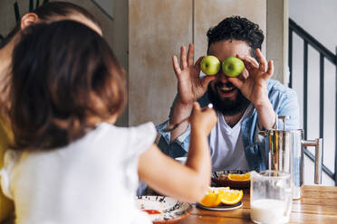 Vater hält Früchte vor den Augen, während er mit seiner Tochter zu Hause spielt - ASGF01001