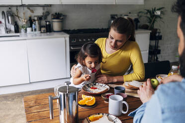 Parents looking at daughter having breakfast at home - ASGF01002