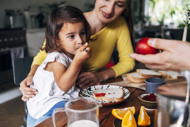 Man giving fruit to daughter having breakfast at home - ASGF01003