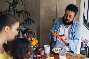 Mann isst Essen, während er mit seiner Familie am Tisch sitzt - ASGF01010