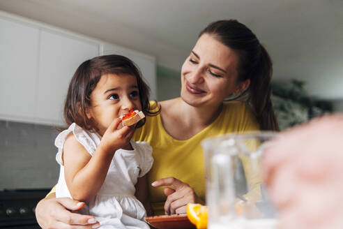 Daughter eating breakfast with mother at home - ASGF01011