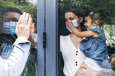 Mann begrüßt Familie durch Glastür während COVID-19 - ASGF01044
