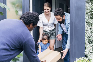 Parents helping daughter receiving package from delivery person at doorway - ASGF01049