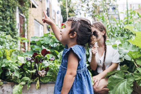 Daughter pointing while standing with mother in background at vegetable garden - ASGF01053