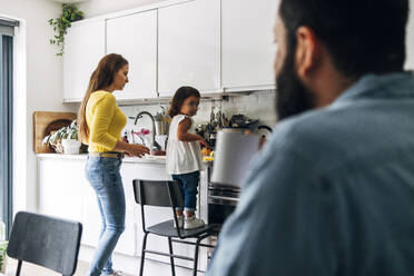 Father looking at daughter helping mother in kitchen - ASGF01062