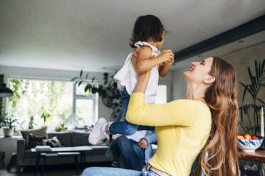 Verspielte Mutter, die ihre Tochter abholt, während sie zu Hause sitzt - ASGF01067