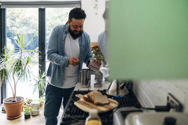 Man preparing coffee while standing at kitchen counter - ASGF01072