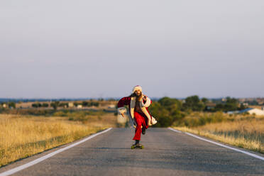 Mann im Weihnachtsmannkostüm fährt bei Sonnenuntergang mit dem Skateboard auf der Straße - OCMF02199