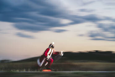 Mann fährt Skateboard auf der Straße und trägt ein Weihnachtsmannkostüm in der Abenddämmerung - OCMF02201