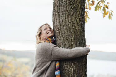 Lächelnde Frau, die einen Baum im Herbst umarmt - JOSEF05345