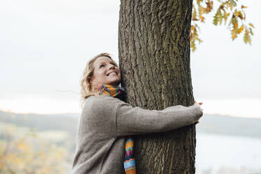 Smiling woman hugging tree during autumn - JOSEF05345