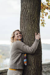 Lächelnde Frau umarmt Baum im Herbst - JOSEF05346