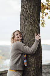 Smiling woman embracing tree during autumn - JOSEF05346