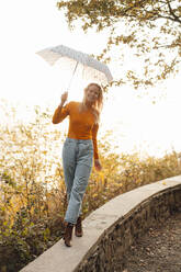 Lächelnde Frau mit Regenschirm auf einer Stützmauer - JOSEF05351