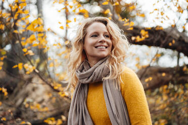 Lächelnde blonde Frau, die vor einem Herbstbaum wegschaut - JOSEF05355