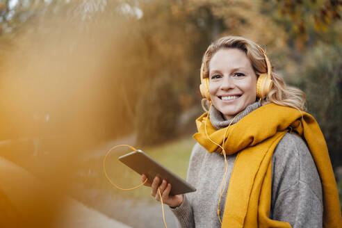 Lächelnde Frau mit digitalem Tablet, die im Herbst Musik hört - JOSEF05357