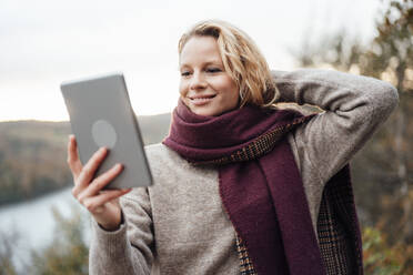 Lächelnde Frau mit Hand hinter dem Kopf, die ein Selfie durch ein digitales Tablet macht - JOSEF05361
