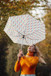 Cheerful woman looking at upside down umbrella - JOSEF05371